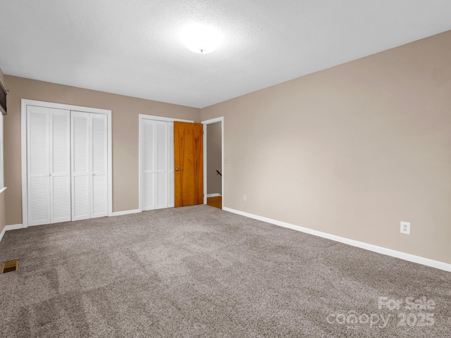 unfurnished bedroom featuring carpet, two closets, and a textured ceiling