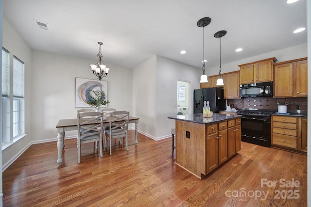 kitchen featuring dark wood-type flooring, tasteful backsplash, a kitchen island, pendant lighting, and black appliances