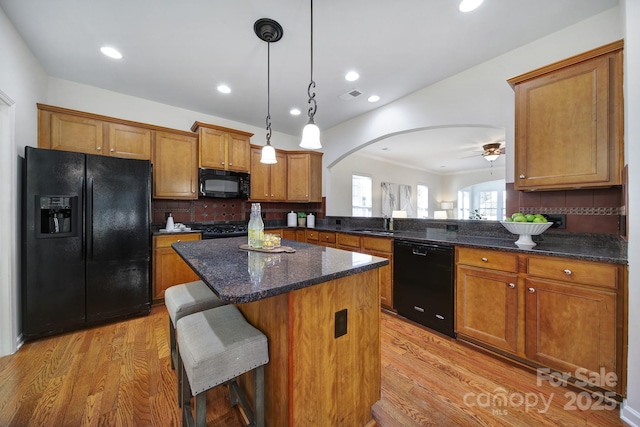 kitchen featuring light hardwood / wood-style flooring, a breakfast bar, hanging light fixtures, black appliances, and kitchen peninsula