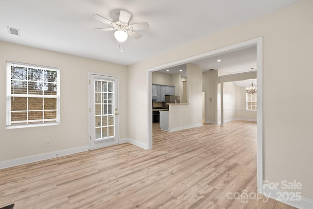 unfurnished living room featuring ceiling fan with notable chandelier and light hardwood / wood-style flooring