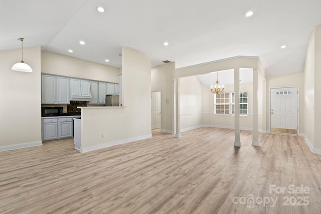 unfurnished living room with lofted ceiling, an inviting chandelier, and light hardwood / wood-style flooring