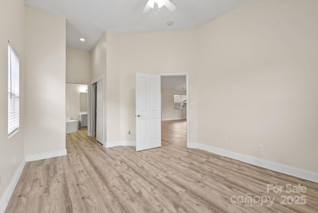 unfurnished bedroom featuring a high ceiling, ceiling fan, light hardwood / wood-style floors, and ensuite bath