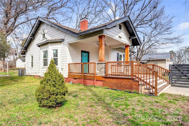 view of front of house featuring central AC unit, ceiling fan, a chimney, a porch, and a front lawn