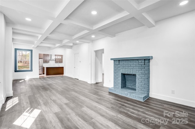 unfurnished living room featuring a brick fireplace, baseboards, coffered ceiling, and wood finished floors