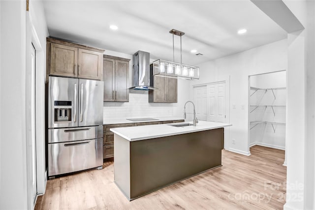 kitchen featuring stainless steel fridge with ice dispenser, wall chimney exhaust hood, black electric cooktop, light wood-style floors, and a sink