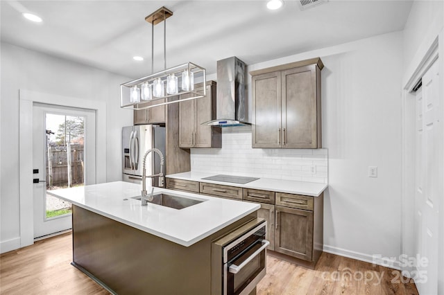 kitchen with decorative backsplash, black electric cooktop, light countertops, wall chimney range hood, and a sink