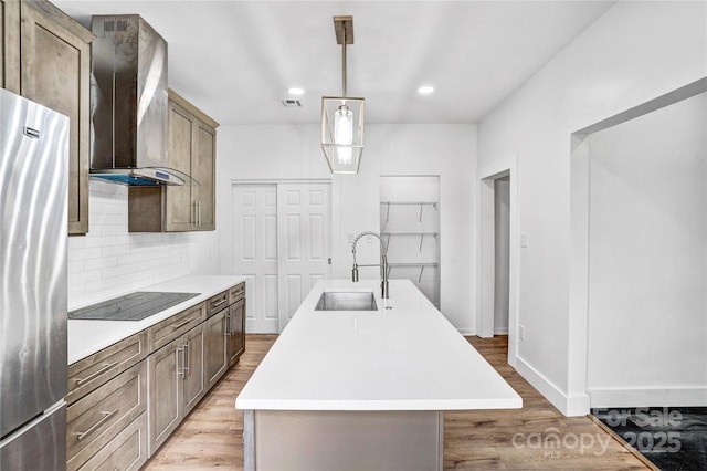 kitchen featuring backsplash, freestanding refrigerator, a sink, wall chimney exhaust hood, and black electric cooktop