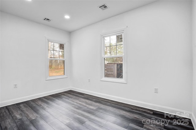 unfurnished room with dark wood-style floors, a healthy amount of sunlight, visible vents, and baseboards