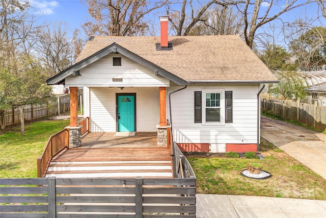 bungalow-style home featuring a chimney, a shingled roof, a porch, a front yard, and fence