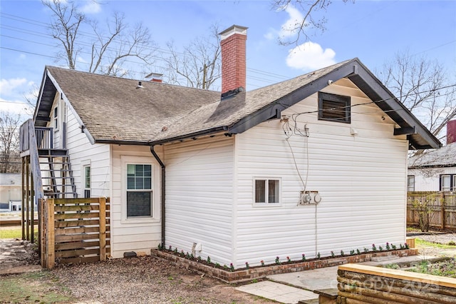 view of property exterior with a shingled roof, fence, a chimney, and stairs