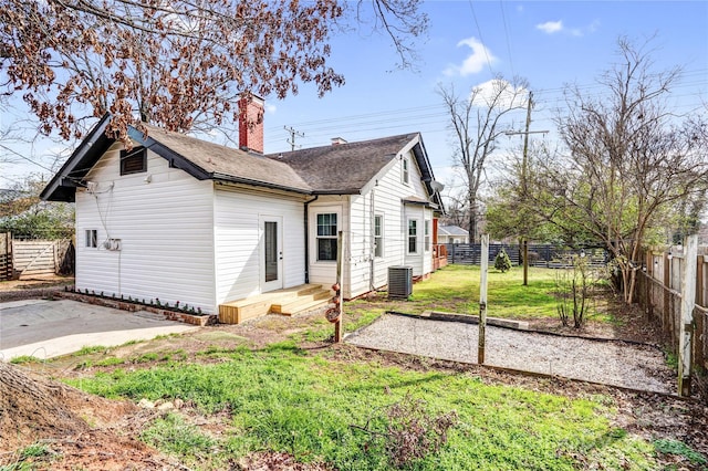 back of house featuring a chimney, a shingled roof, a lawn, fence, and cooling unit