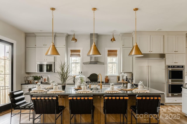 kitchen featuring a breakfast bar, appliances with stainless steel finishes, a center island, decorative light fixtures, and wall chimney exhaust hood