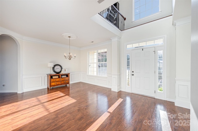 entrance foyer featuring dark wood-style floors, arched walkways, visible vents, an inviting chandelier, and ornamental molding