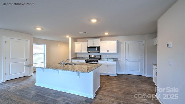 kitchen with appliances with stainless steel finishes, a kitchen island with sink, white cabinets, and a kitchen bar