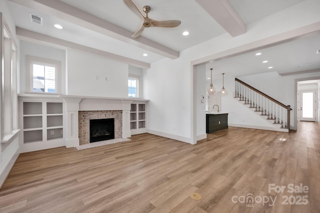 unfurnished living room with light wood-style flooring, visible vents, baseboards, stairway, and beamed ceiling