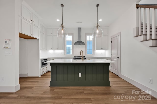 kitchen with light countertops, wall chimney range hood, light wood-style flooring, and white cabinets