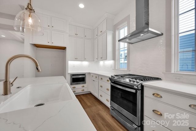 kitchen with stainless steel gas range oven, white cabinets, wall chimney exhaust hood, a sink, and backsplash