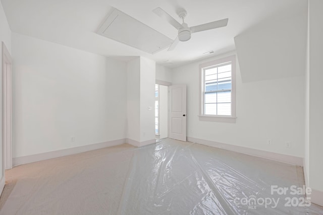 empty room with a ceiling fan, attic access, and baseboards