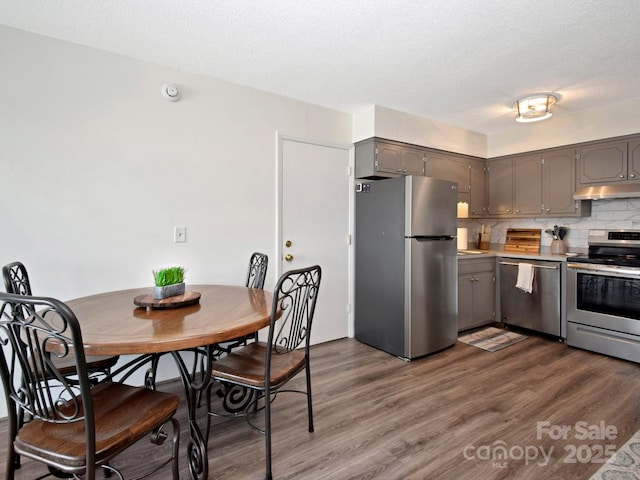 kitchen featuring appliances with stainless steel finishes, gray cabinetry, dark hardwood / wood-style floors, tasteful backsplash, and a textured ceiling