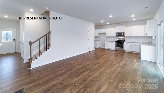 kitchen with light stone counters, dark wood-type flooring, white cabinets, and appliances with stainless steel finishes