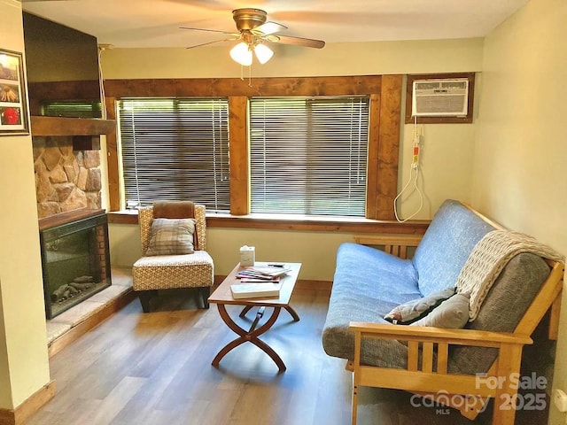 living area featuring ceiling fan, a stone fireplace, a wall mounted air conditioner, and wood-type flooring