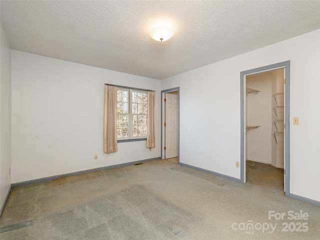 unfurnished bedroom with a spacious closet, light carpet, and a textured ceiling