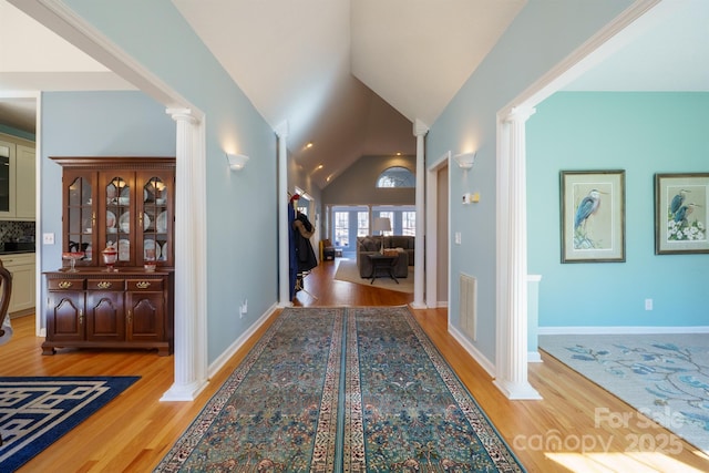 corridor with ornate columns, vaulted ceiling, and light hardwood / wood-style floors