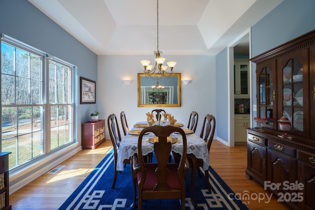 dining area with an inviting chandelier, a tray ceiling, and light hardwood / wood-style floors