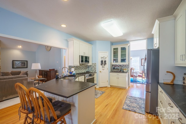 kitchen with sink, light hardwood / wood-style flooring, appliances with stainless steel finishes, decorative backsplash, and white cabinets