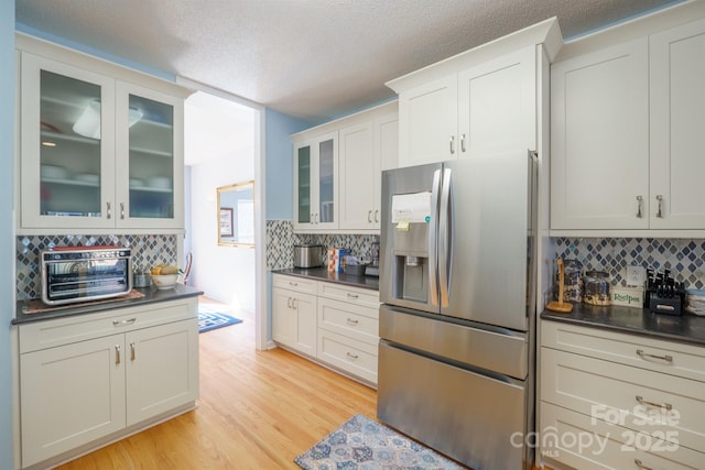 kitchen featuring tasteful backsplash, white cabinetry, a textured ceiling, stainless steel fridge, and light hardwood / wood-style floors