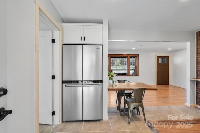 kitchen with stainless steel refrigerator, light tile patterned floors, and white cabinets