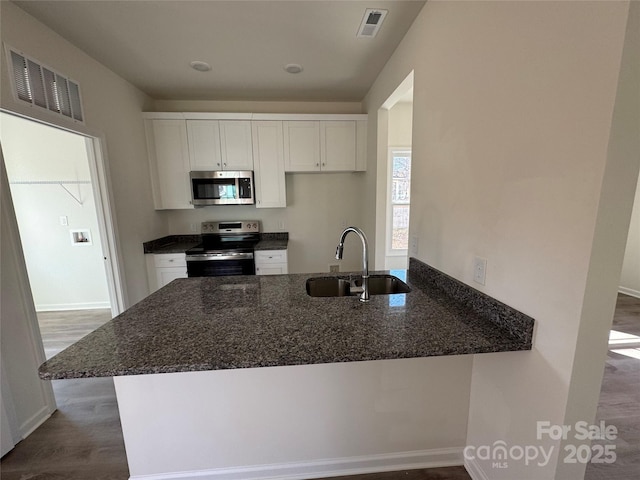 kitchen featuring a peninsula, a sink, visible vents, appliances with stainless steel finishes, and dark stone counters