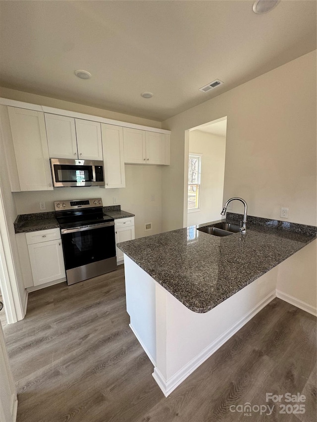 kitchen featuring dark wood finished floors, visible vents, appliances with stainless steel finishes, a sink, and a peninsula