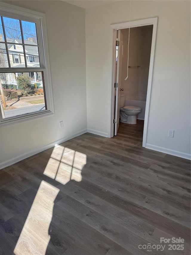 unfurnished bedroom with dark wood finished floors, connected bathroom, and baseboards