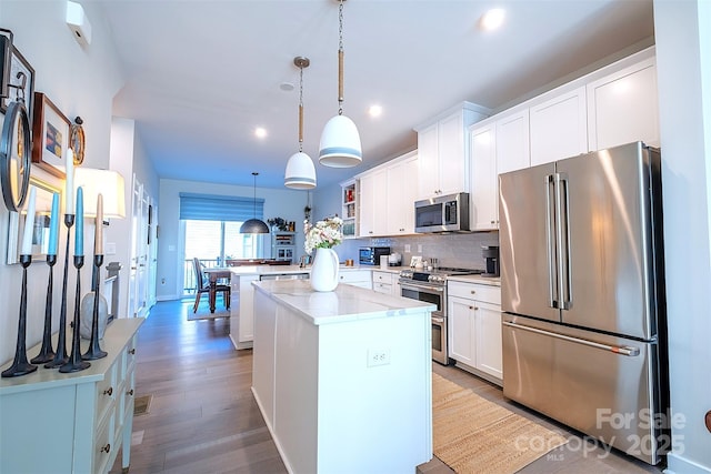 kitchen featuring a kitchen island, white cabinetry, appliances with stainless steel finishes, and decorative light fixtures