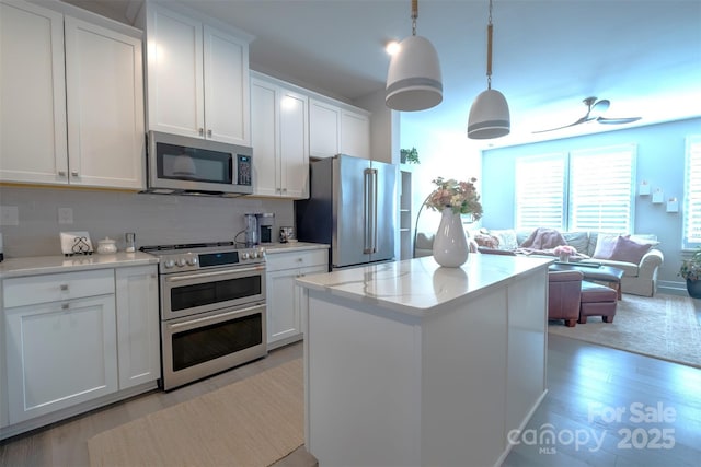 kitchen with hanging light fixtures, backsplash, stainless steel appliances, white cabinets, and light wood-type flooring