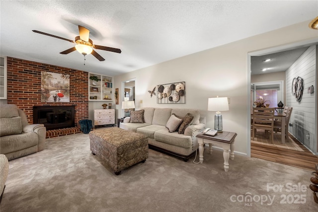 carpeted living room with ceiling fan, a fireplace, built in features, and a textured ceiling