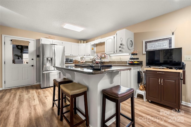 kitchen featuring white cabinetry, stainless steel appliances, a kitchen bar, and light wood-type flooring