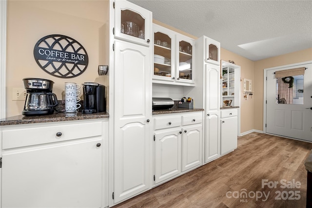 kitchen featuring dark stone countertops, a textured ceiling, light hardwood / wood-style floors, and white cabinets