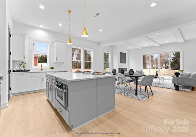 kitchen featuring pendant lighting, white cabinetry, a center island, stainless steel oven, and light wood-type flooring