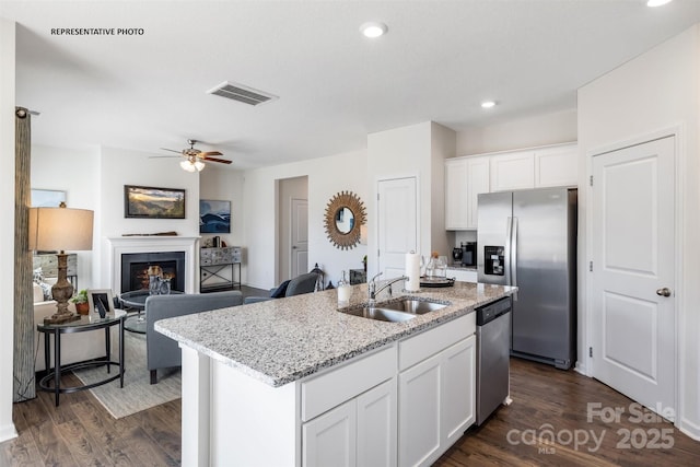 kitchen with sink, dark wood-type flooring, appliances with stainless steel finishes, white cabinets, and a center island with sink