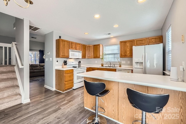 kitchen featuring sink, white appliances, wood-type flooring, a kitchen bar, and kitchen peninsula