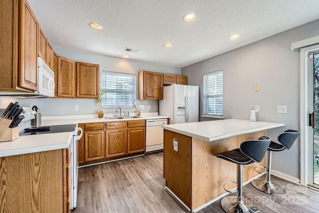 kitchen with sink, white appliances, light hardwood / wood-style flooring, a kitchen breakfast bar, and kitchen peninsula