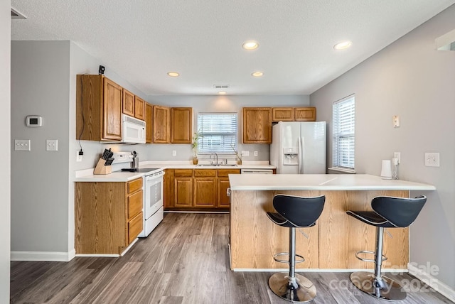 kitchen with white appliances, dark hardwood / wood-style floors, a healthy amount of sunlight, and a kitchen bar