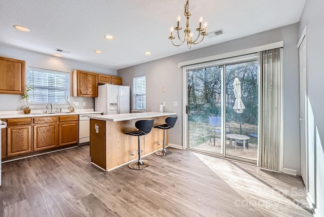 kitchen with a kitchen island, decorative light fixtures, a breakfast bar area, white appliances, and light hardwood / wood-style flooring