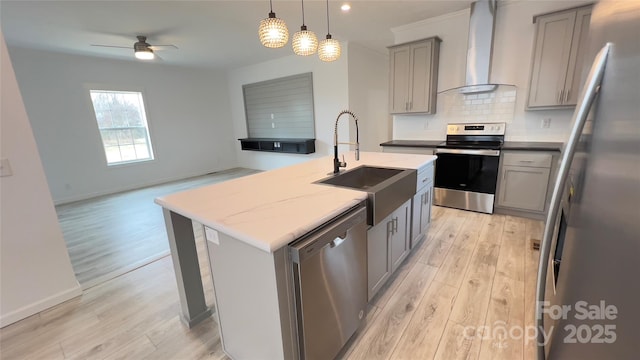 kitchen with a kitchen island with sink, stainless steel appliances, a sink, wall chimney range hood, and gray cabinets