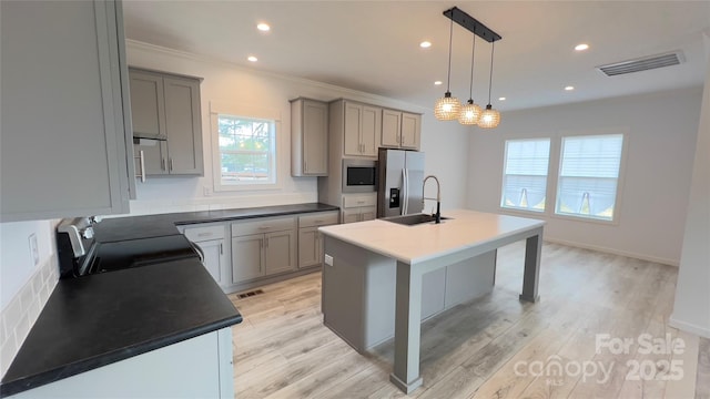 kitchen featuring decorative light fixtures, gray cabinets, appliances with stainless steel finishes, a sink, and an island with sink