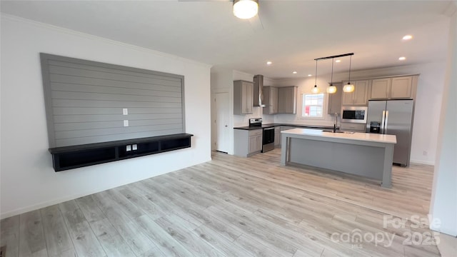 kitchen with decorative light fixtures, a center island with sink, light countertops, appliances with stainless steel finishes, and wall chimney range hood