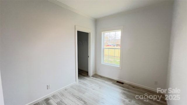 unfurnished room with light wood-style floors, visible vents, ornamental molding, and baseboards