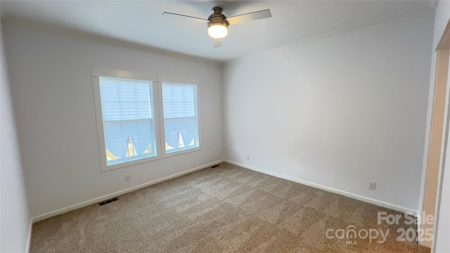 carpeted empty room featuring baseboards, crown molding, visible vents, and a ceiling fan